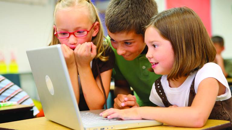 Three young students crowd around a laptop computer