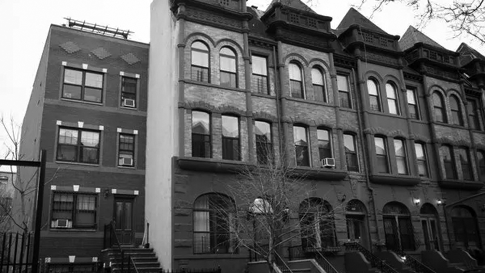 A black-and-white photo of a tenement building featuring a row of connected homes. 