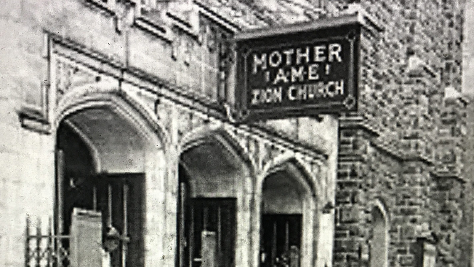 A black-and-white exterior photo of a building. The photo features a sign naming the building “Mother A.M.E. Zion Church.”   