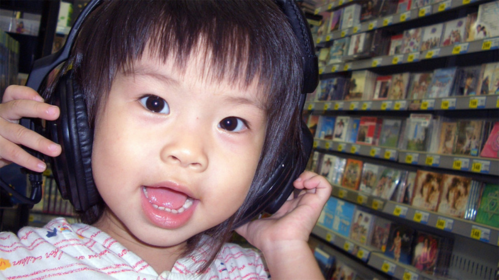 A photo of a child wearing headphones while standing next to a wall of CDs.